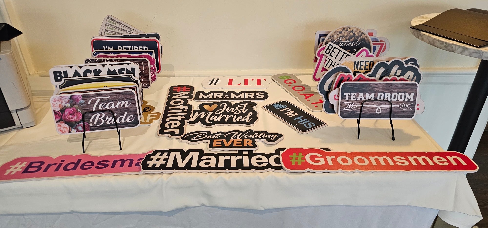 Table displaying wedding photo booth props including Team Bride and Groom signs and hashtags.