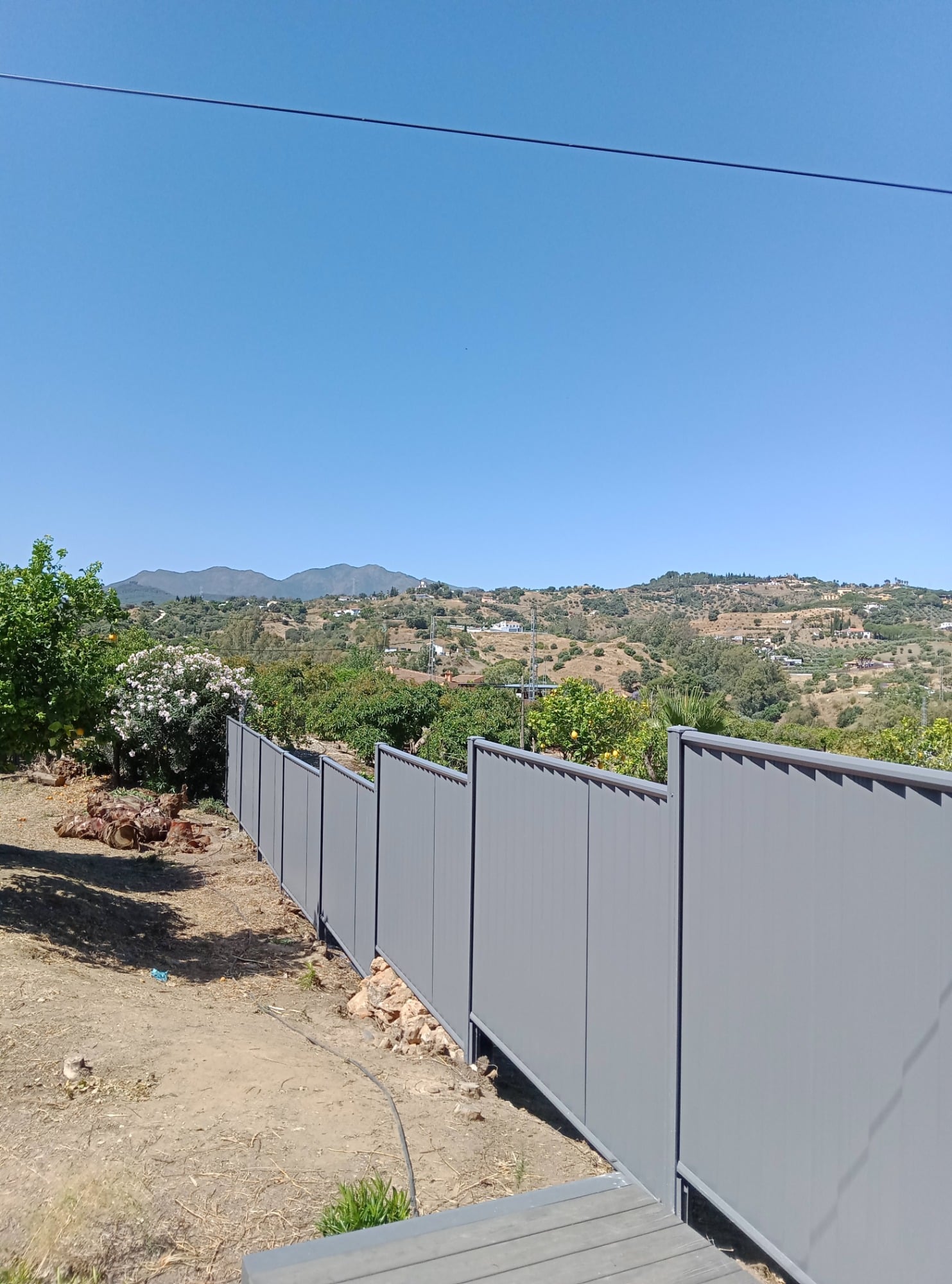Grey ColourFence steel fencing installed along a sloping garden boundary. The vertical steel panels provide an attractive